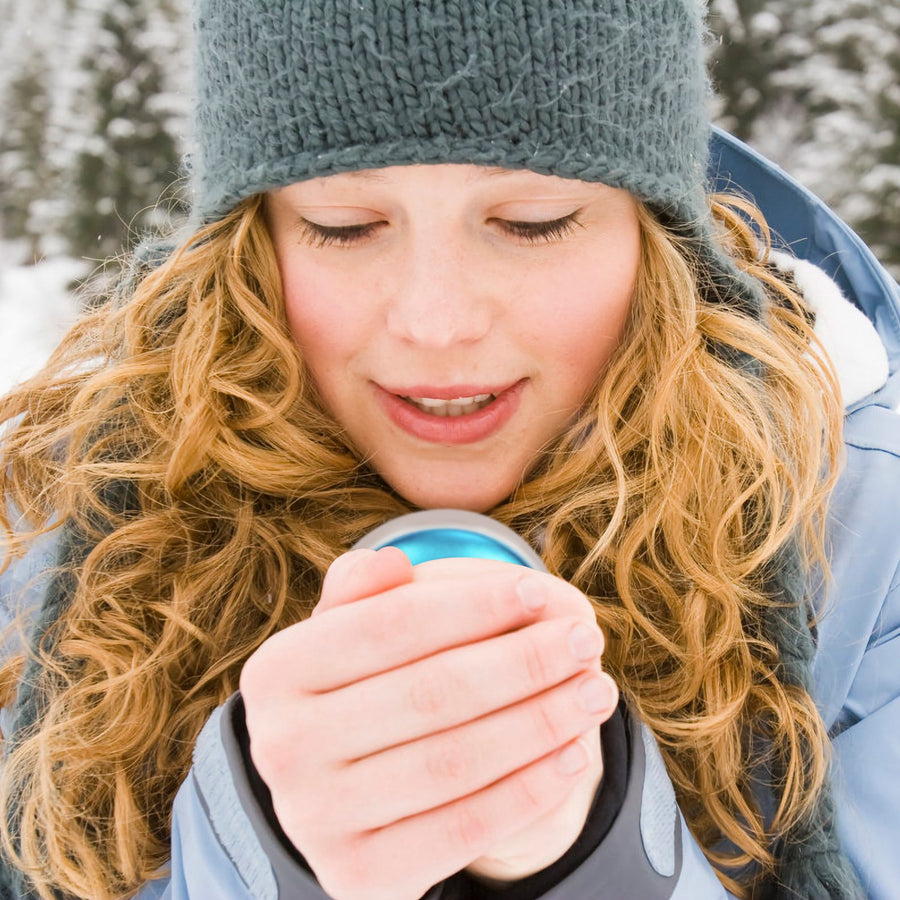 Woman warming her hands with the blue rechargeable hand warmer outdoors in the snow